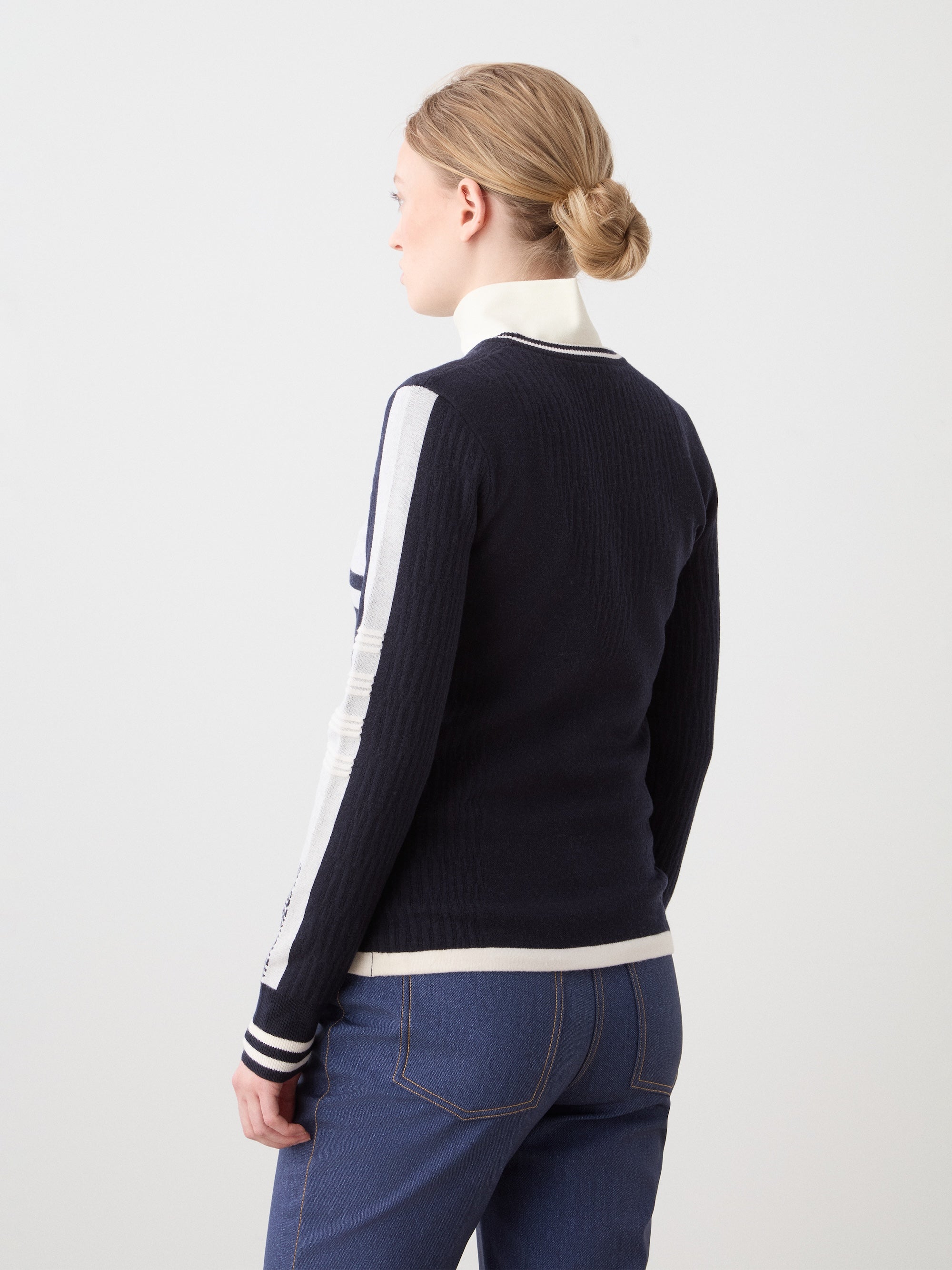 We Norwegians | FW25 | Womens Rocky Ski Sweater_Navy blue | Model wearing this mid-weight knit designed in a retro style with a round neckline and contrasting color block panels on the chest and sleeves - paired with the Western ski pants | Shot against an off-white background | Back
