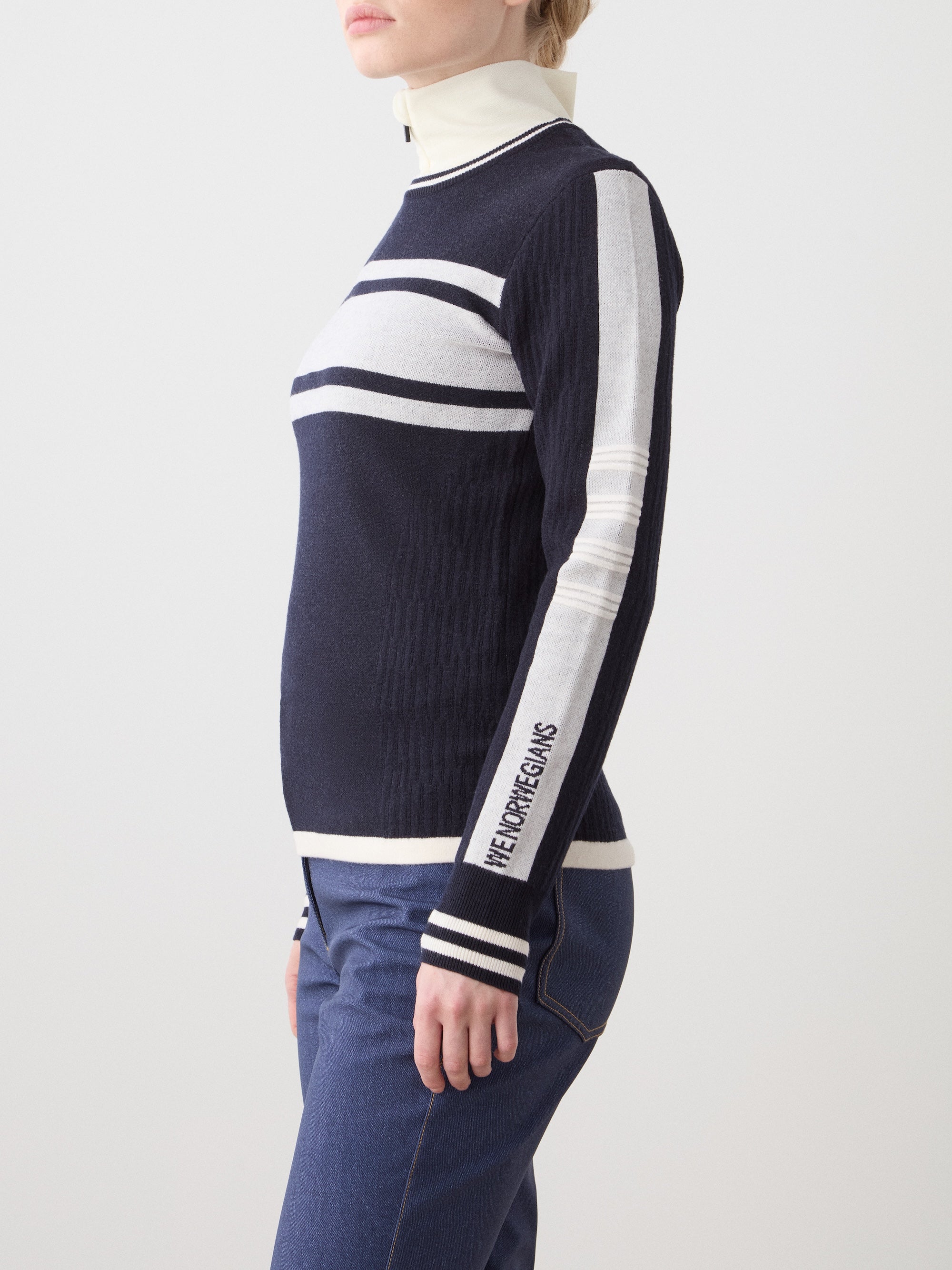 We Norwegians | FW25 | Womens Rocky Ski Sweater_Navy blue | Model wearing this mid-weight knit designed in a retro style with a round neckline and contrasting color block panels on the chest and sleeves - paired with the Western ski pants | Shot against an off-white background | Side/ Close-up