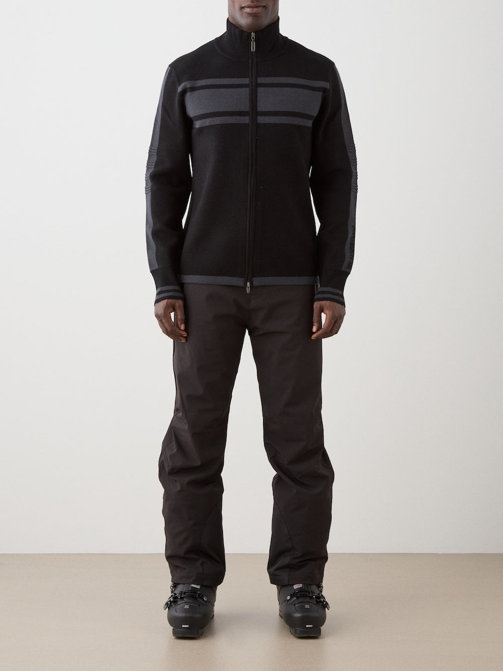 We Norwegians | FW25 | Mens Rocky Full ZipUp_Black | Model wearing this fine knitted sweater with a 2-way front zipper opening, designed in a retro style with subtle color blocks on the chest and sleeves - paired with black ski pants | Shot against an off-white background | Front