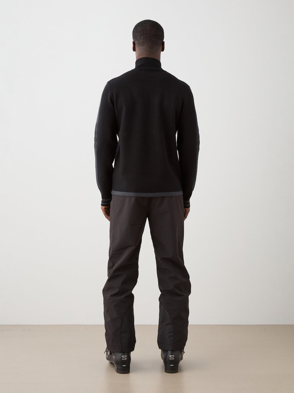 We Norwegians | FW25 | Mens Rocky Full ZipUp_Black | Model wearing this fine knitted sweater with a 2-way front zipper opening, designed in a retro style with subtle color blocks on the chest and sleeves - paired with black ski pants | Shot against an off-white background | Back