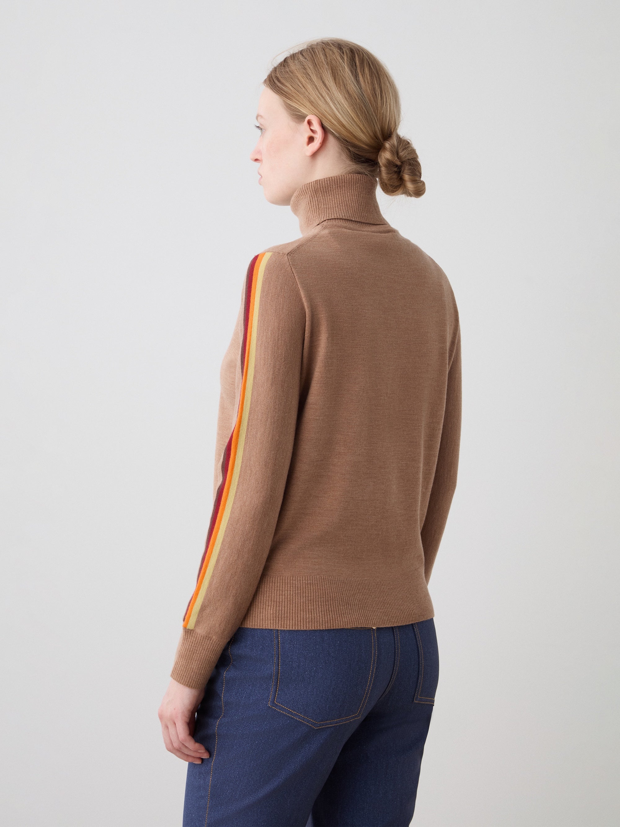 We Norwegians | FW25 | Womens Freebird Turtleneck Sweater_Cinnamon | Model is wearing this knitted turtleneck sweater with contrasting panels on the sleeves - paired with the Western ski pants | Shot against an off-white background | Back