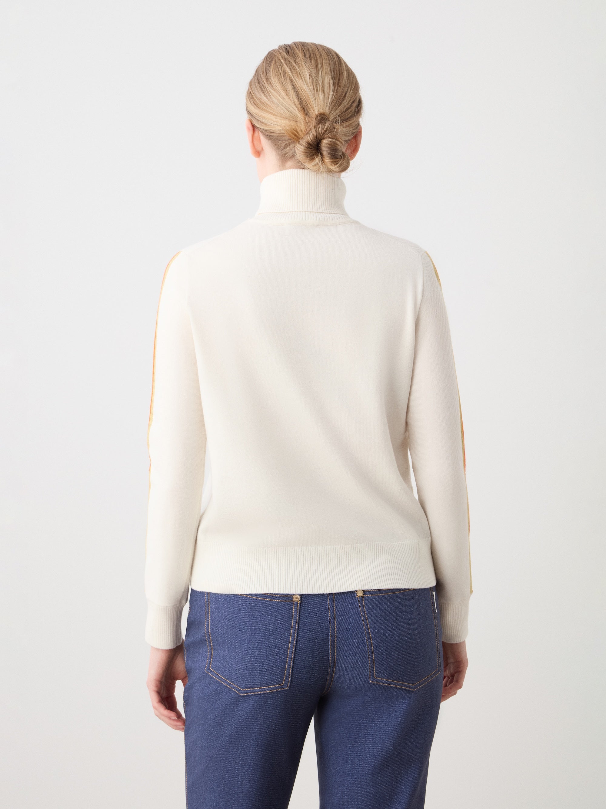 We Norwegians | FW25 | Womens Freebird Turtleneck Sweater_Off-white | Model is wearing this knitted turtleneck sweater with contrasting panels on the sleeves - paired with the Western ski pants | Shot against an off-white background | Back