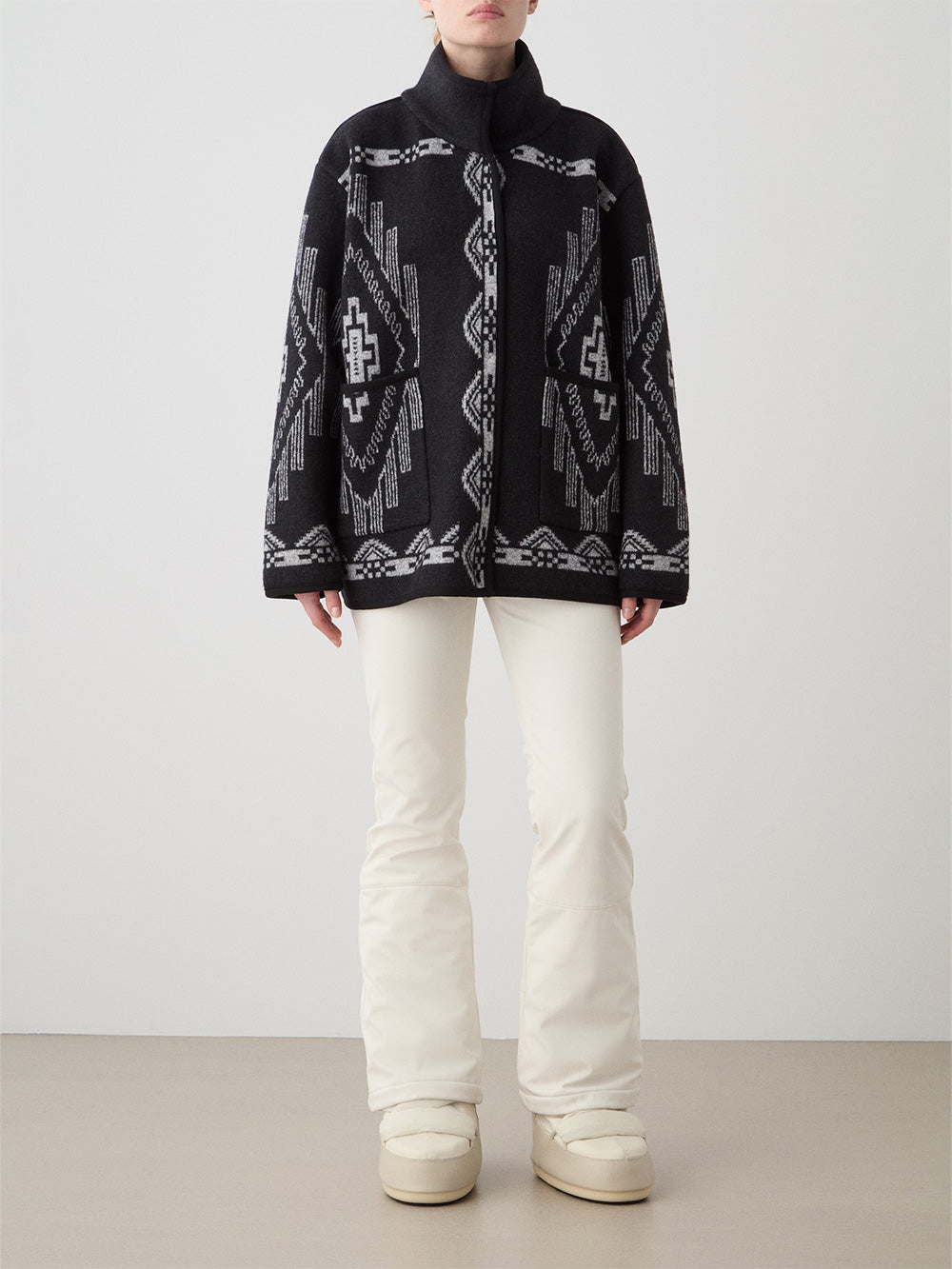 We Norwegians_FW25_Womens | Model is wearing the Black Kautokeino jacket with Off white Tyin Bootleg Ski pants | The jacket come with a jacquard pattern inspired by Native and Indigenous American art | Front view against a white background