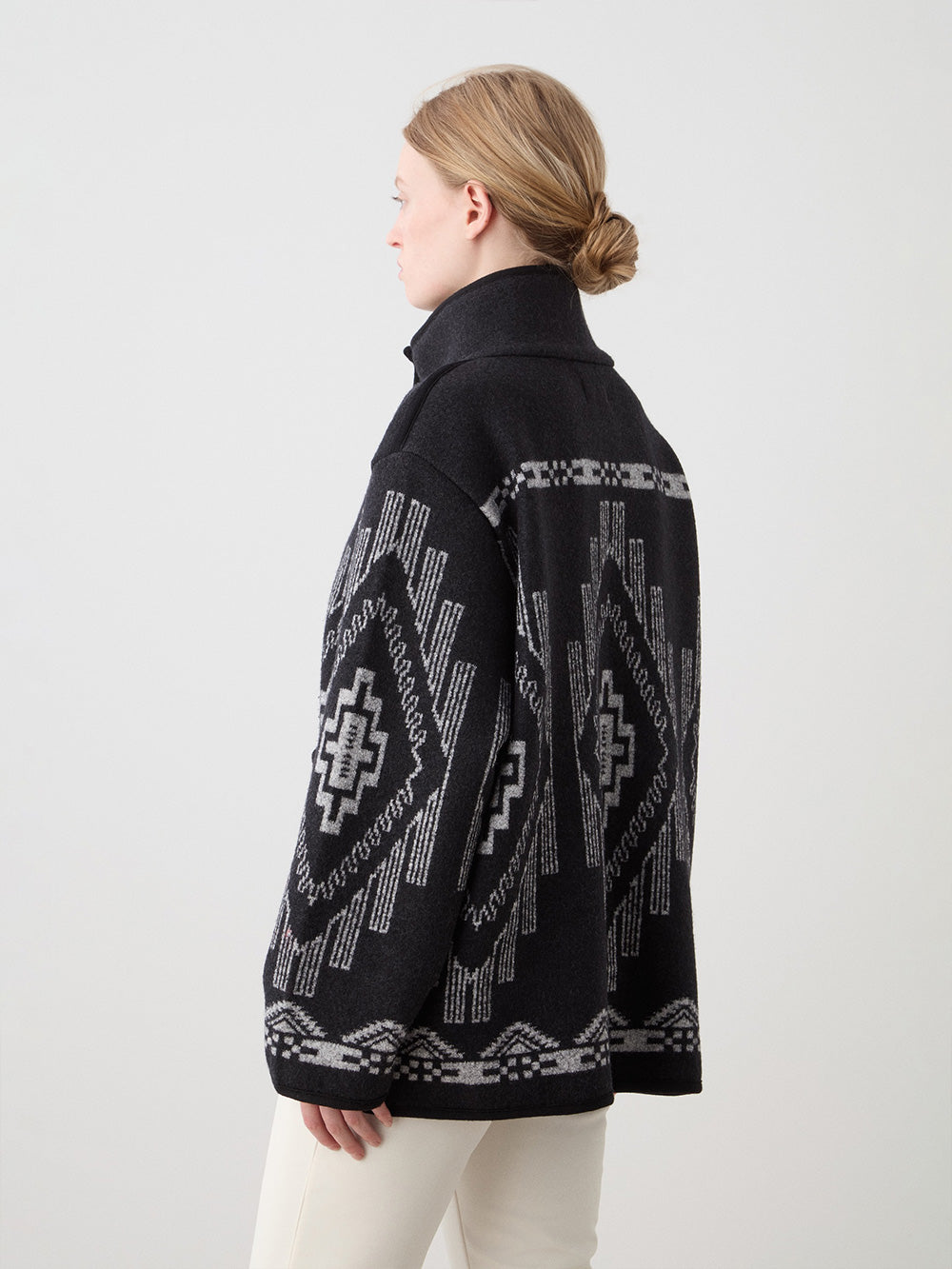 We Norwegians_FW25_Womens | Model is wearing the Black Kautokeino jacket with Off white Tyin Bootleg Ski pants | The jacket come with a jacquard pattern inspired by Native and Indigenous American art | Back view against a white background