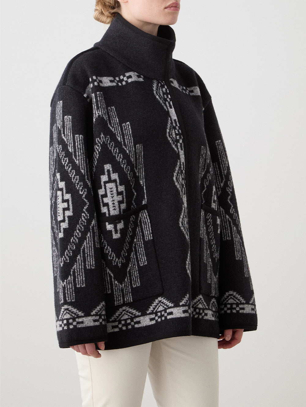 We Norwegians_FW25_Womens | Model is wearing the Black Kautokeino jacket with Off white Tyin Bootleg Ski pants | The jacket come with a jacquard pattern inspired by Native and Indigenous American art | Photograph showing the pattern details of the garment against a white background