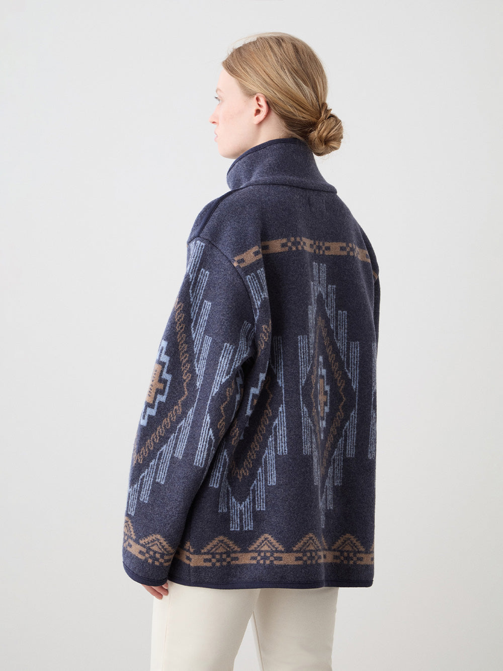 We Norwegians_FW25_Womens | Model is wearing the Navy blue Kautokeino jacket with Off white Tyin Bootleg Ski pants | The jacket come with a jacquard pattern inspired by Native and Indigenous American art | Back view against a white background