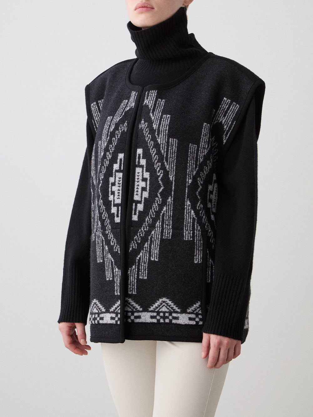 We Norwegians_FW25_Women | Model is wearing the Kautokeino vest | Black in color with a jacquard pattern inspired by Native and Indigenous American Art | Vest has a matching belt to cinch the waist | Photograph shows the details of the garment on a white background