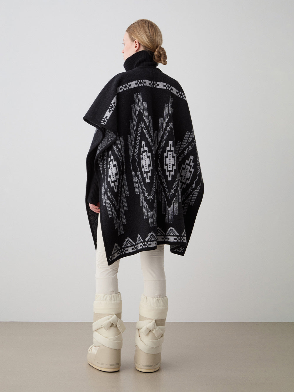 We Norwegians_FW25_Model is wearing the Kautokeino poncho | Black in color with a jacquard pattern inspired by Native and Indigenous American art | Made with boiled merino wool | Back view