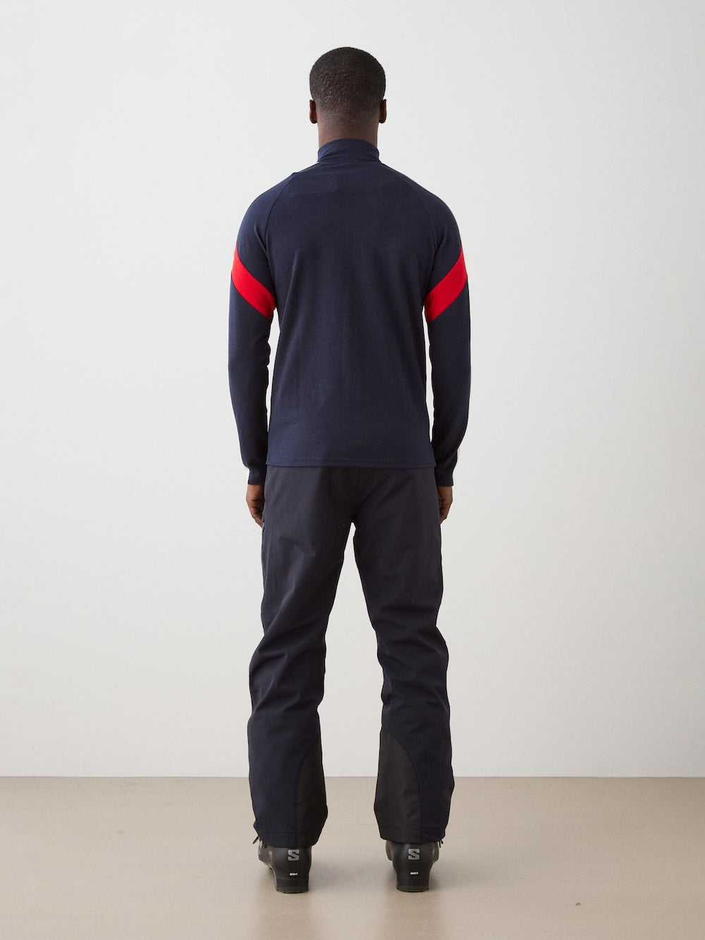 We Norwegians | FW25 | Mens Zermatt Full Zip Sweater_Flag | The model is wearing this piqué knit sweater with white and red accents on the sleeves and a front 2-way zipper opening - paired with black ski pants | Shot against an off-white background | Back