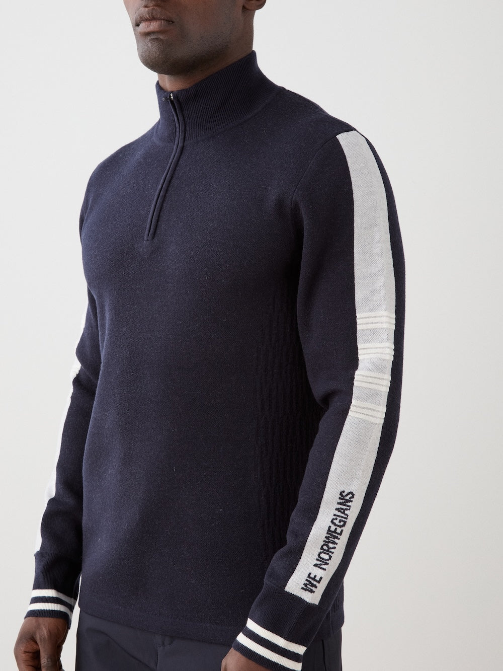 We Norwegians | FW25 | Mens Rocky ZipUp_Navy blue | The model is wearing this knitted sweater designed in a retro style with a front 1/4th zipper opening, color block panels on the sleeves, with embroidered branding | Close-up