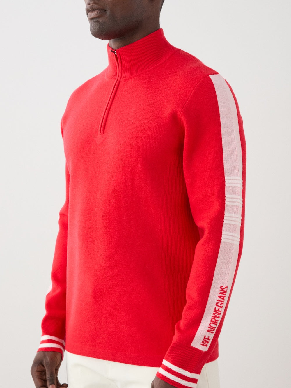 We Norwegians | FW25 | Mens Rocky ZipUp_Red | The model is wearing this knitted sweater designed in a retro style with a front 1/4th zipper opening, color block panels on the sleeves, with embroidered branding | Close-up