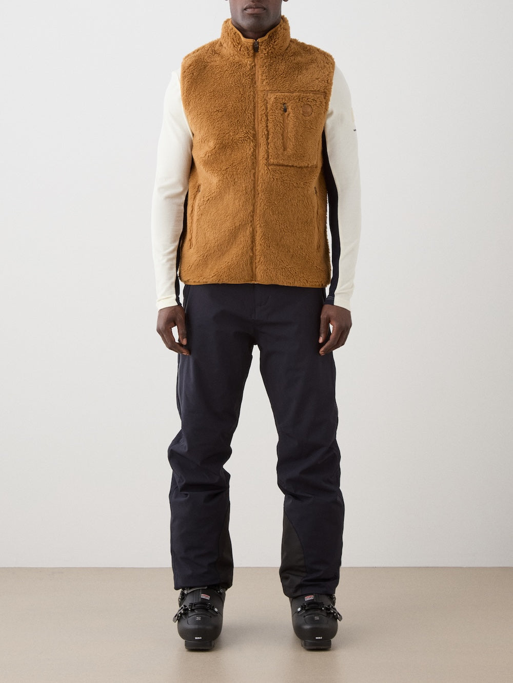 We Norwegians | FW25 | Mens Kebnekaise Vest_Cinnamon | Model wearing this fleece vest with front zipper opening, zipped chest pocket and side pockets -over an off-white top - paired with black ski pants | Shot against an off-white background | Front