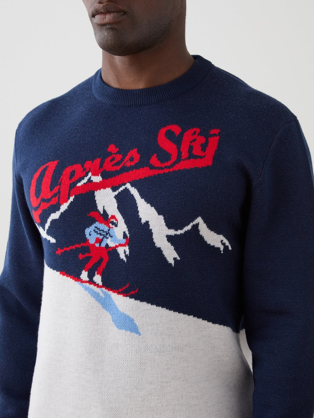 We Norwegians | FW25 | Mens Afterski Crewneck_Navy blue | Model wearing a knitted sweater with an après ski design at the front | Shot against an off-white background | Close-up view