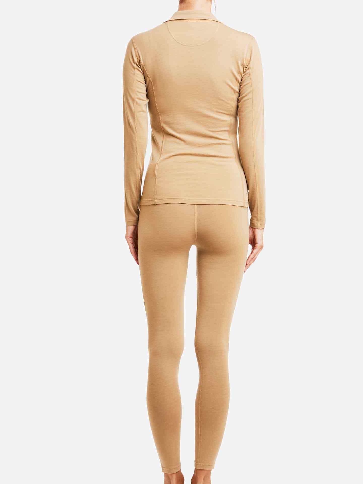 A person is standing facing away from the camera, wearing a fitted beige long-sleeve top and matching leggings, epitomizing Scandinavian luxury base-layers with its super fine merino wool construction. The ensemble is identified as the "Sno Merino Zip Up Women" by We Norwegians. The background is plain white.