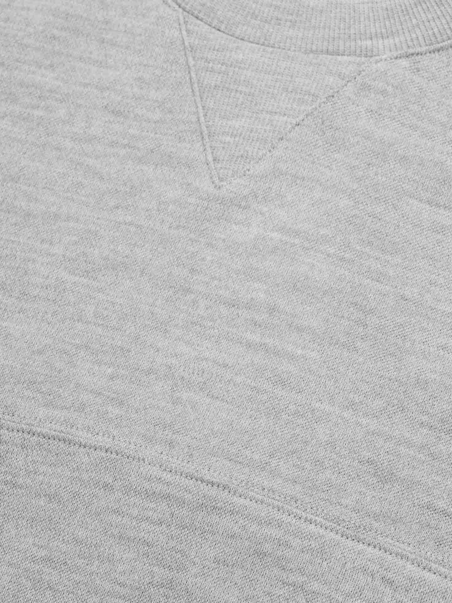 Close-up image of We Norwegians' Tind Crewneck Men, highlighting the texture and stitching details of its gray Merino wool fabric. The image showcases a triangle-shaped ribbed detail near the neckline and horizontal seam lines, emphasizing the soft and comfortable quality typical of casual sportswear.