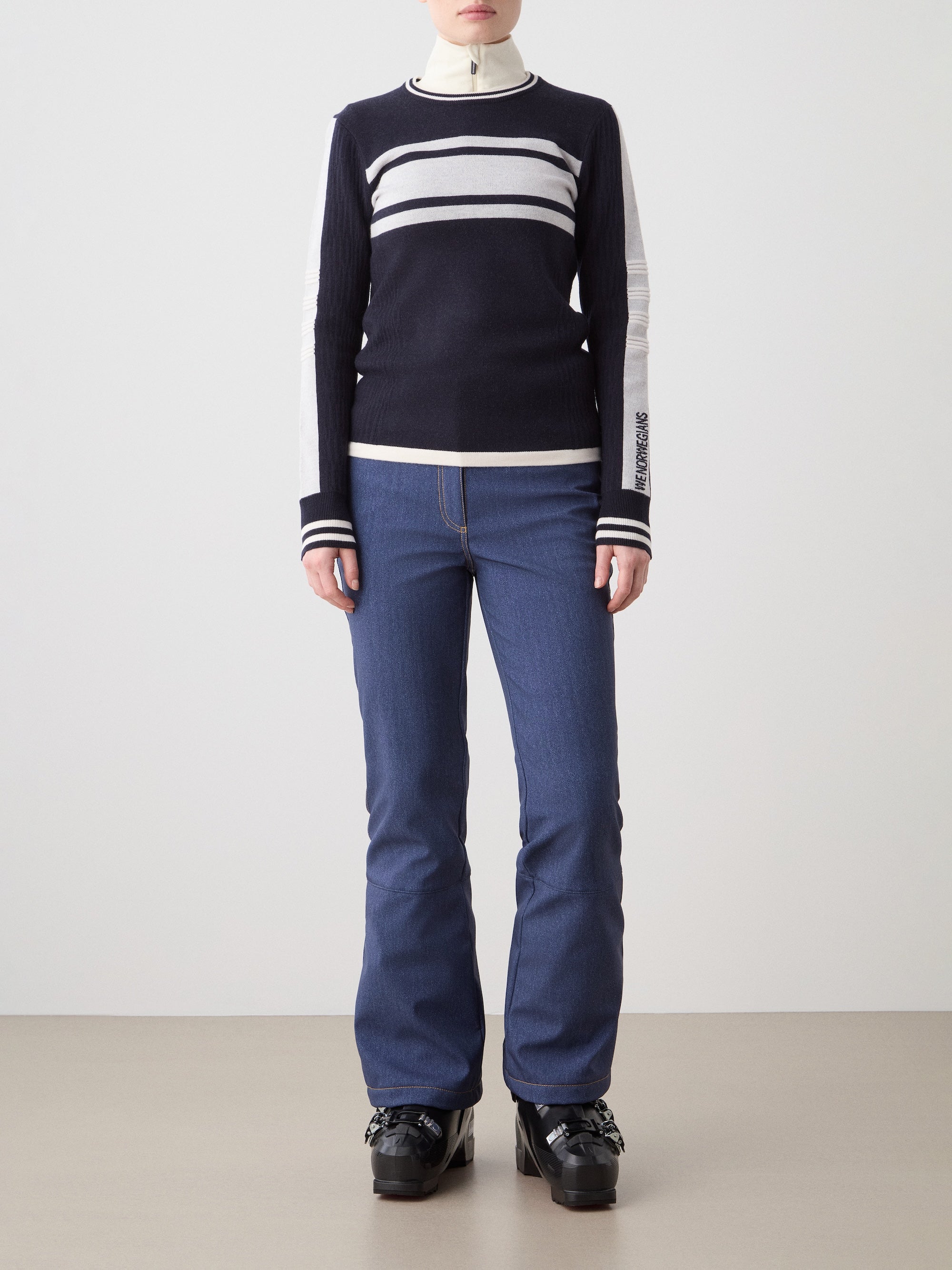 We Norwegians | FW25 | Womens Rocky Ski Sweater_Navy blue | Model wearing this mid-weight knit designed in a retro style with a round neckline and contrasting color block panels on the chest and sleeves - paired with the Western ski pants | Shot against an off-white background | Front