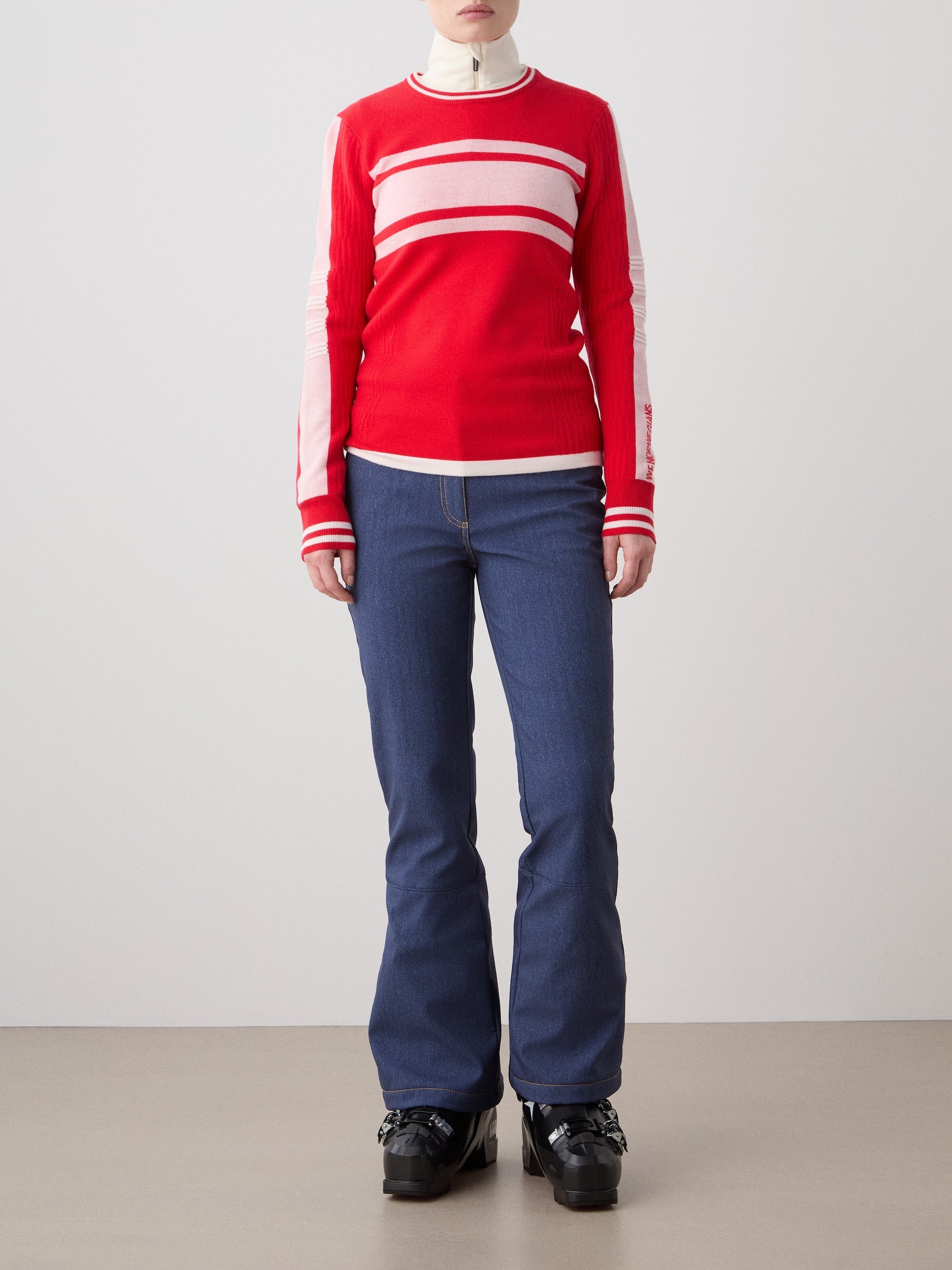 We Norwegians | FW25 | Womens Rocky Ski Sweater_Red | Model wearing this mid-weight knit designed in a retro style with a round neckline and contrasting color block panels on the chest and sleeves - paired with the Western ski pants | Shot against an off-white background | Front