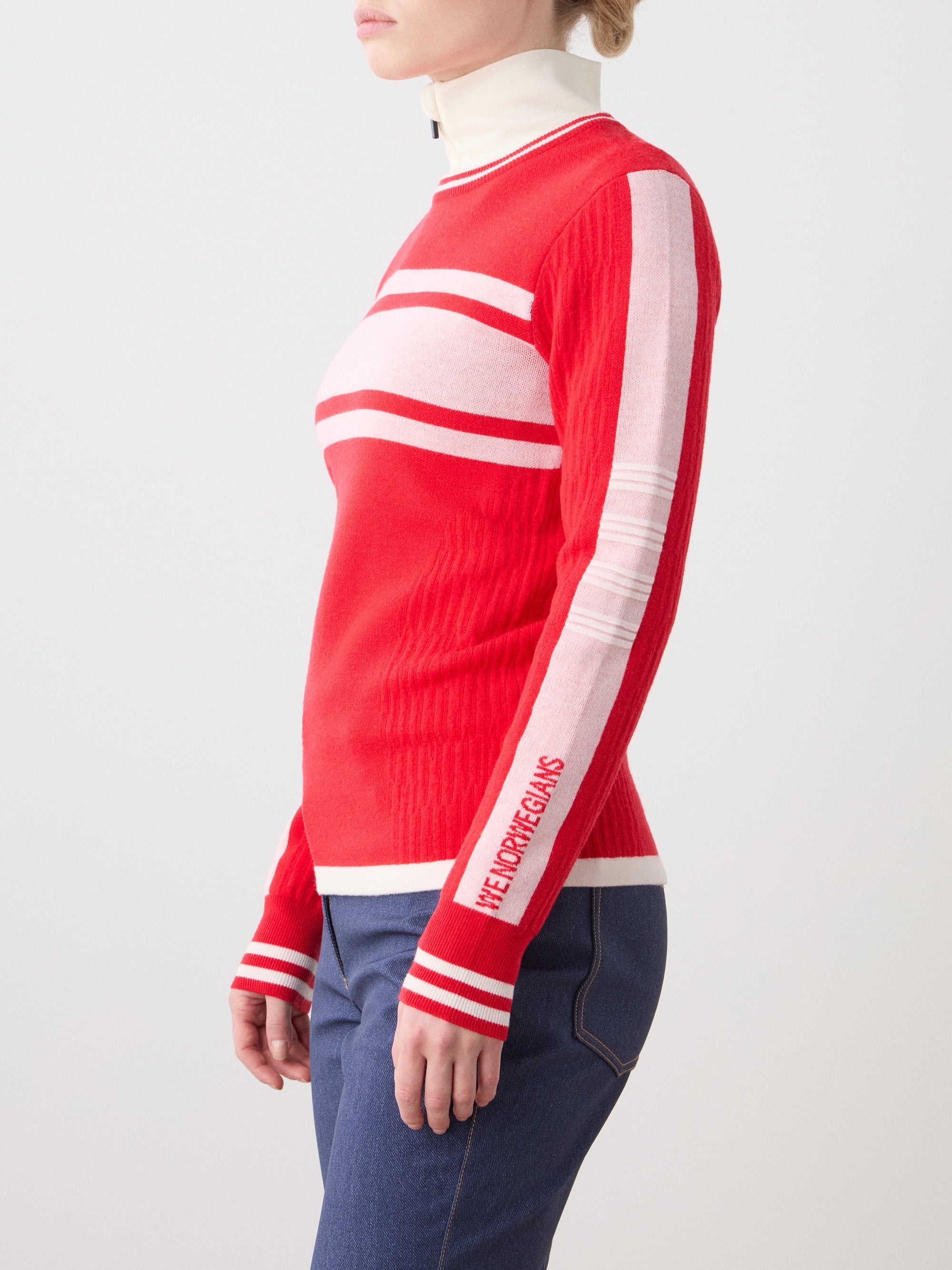 We Norwegians | FW25 | Womens Rocky Ski Sweater_Red | Model wearing this mid-weight knit designed in a retro style with a round neckline and contrasting color block panels on the chest and sleeves - paired with the Western ski pants | Shot against an off-white background | Side/ Close-up