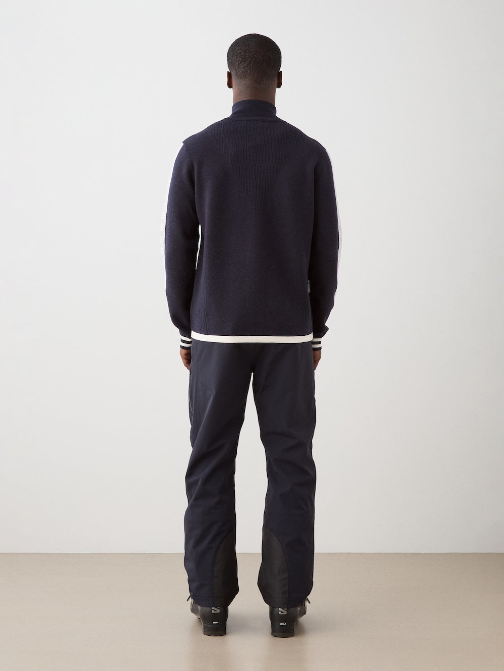 We Norwegians | FW25 | Mens Rocky Full ZipUp_Navy blue | Model wearing this fine knitted sweater with a 2-way front zipper opening, designed in a retro style with contrasting color blocks on the chest and sleeves - paired with black ski pants | Shot against an off-white background | Back