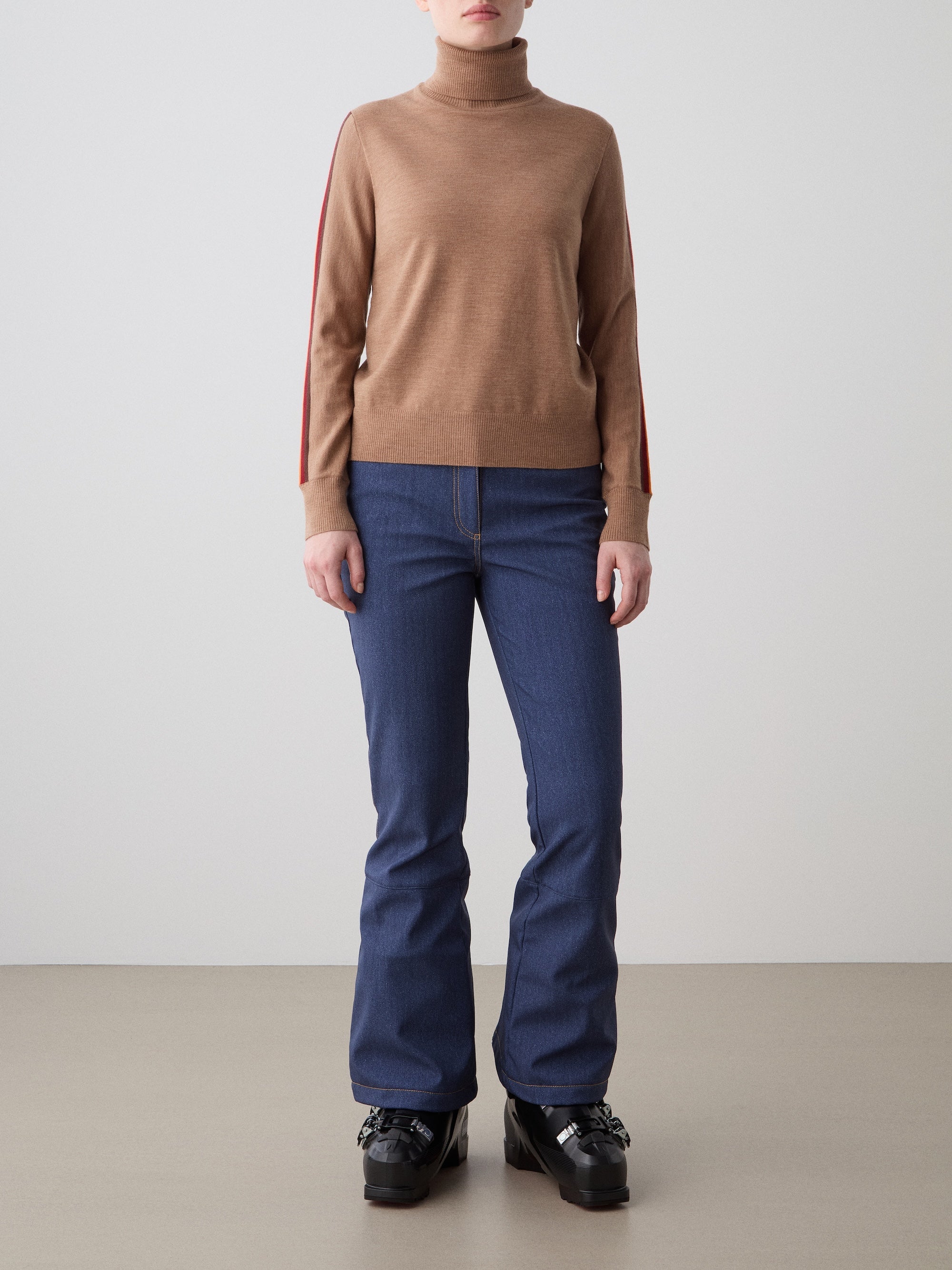 We Norwegians | FW25 | Womens Freebird Turtleneck Sweater_Cinnamon | Model is wearing this knitted turtleneck sweater with contrasting panels on the sleeves - paired with the Western ski pants | Shot against an off-white background | Front