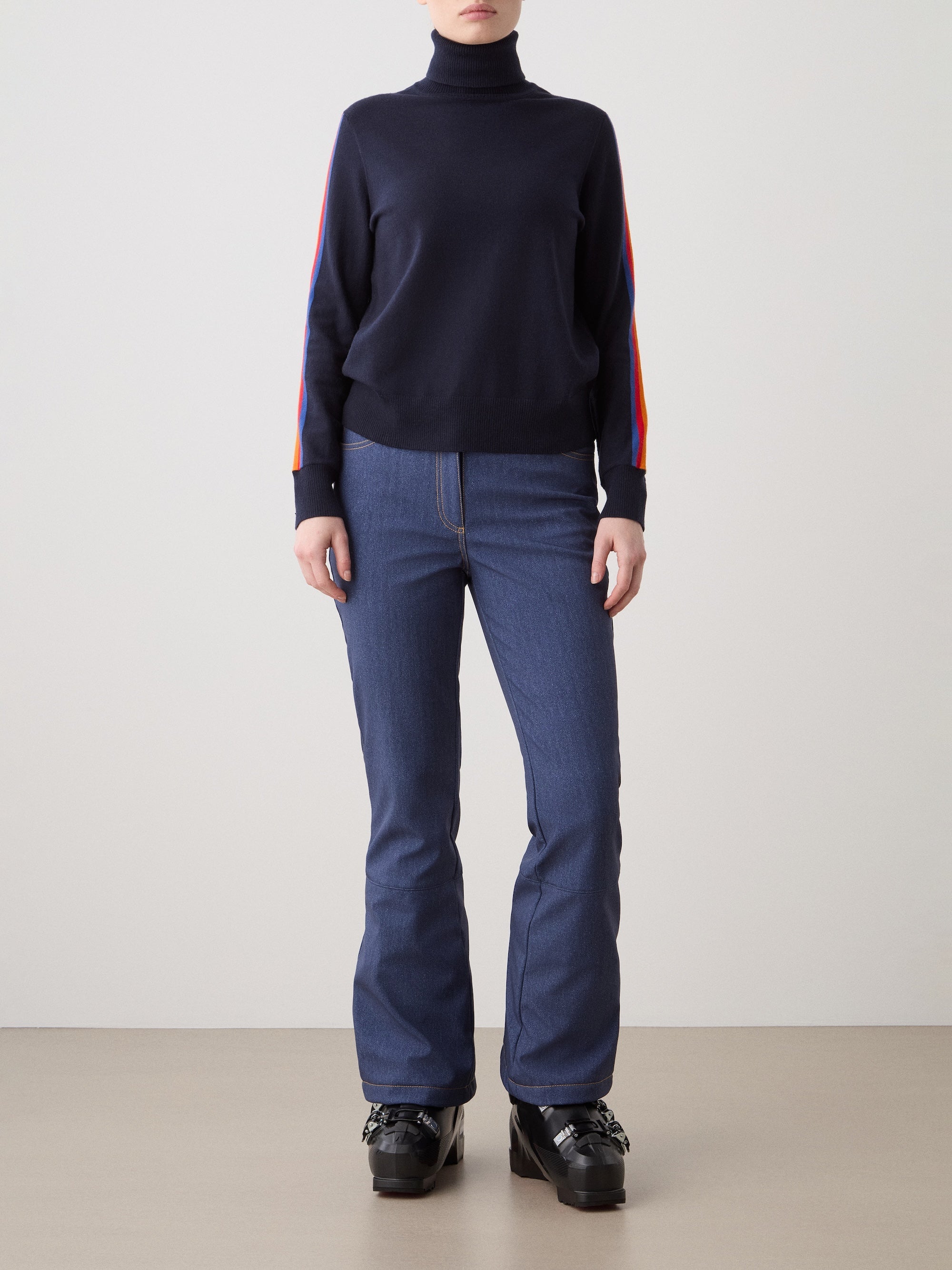 We Norwegians | FW25 | Womens Freebird Turtleneck Sweater_Navy blue | Model is wearing this knitted turtleneck sweater with contrasting panels on the sleeves - paired with the Western ski pants | Shot against an off-white background | Front
