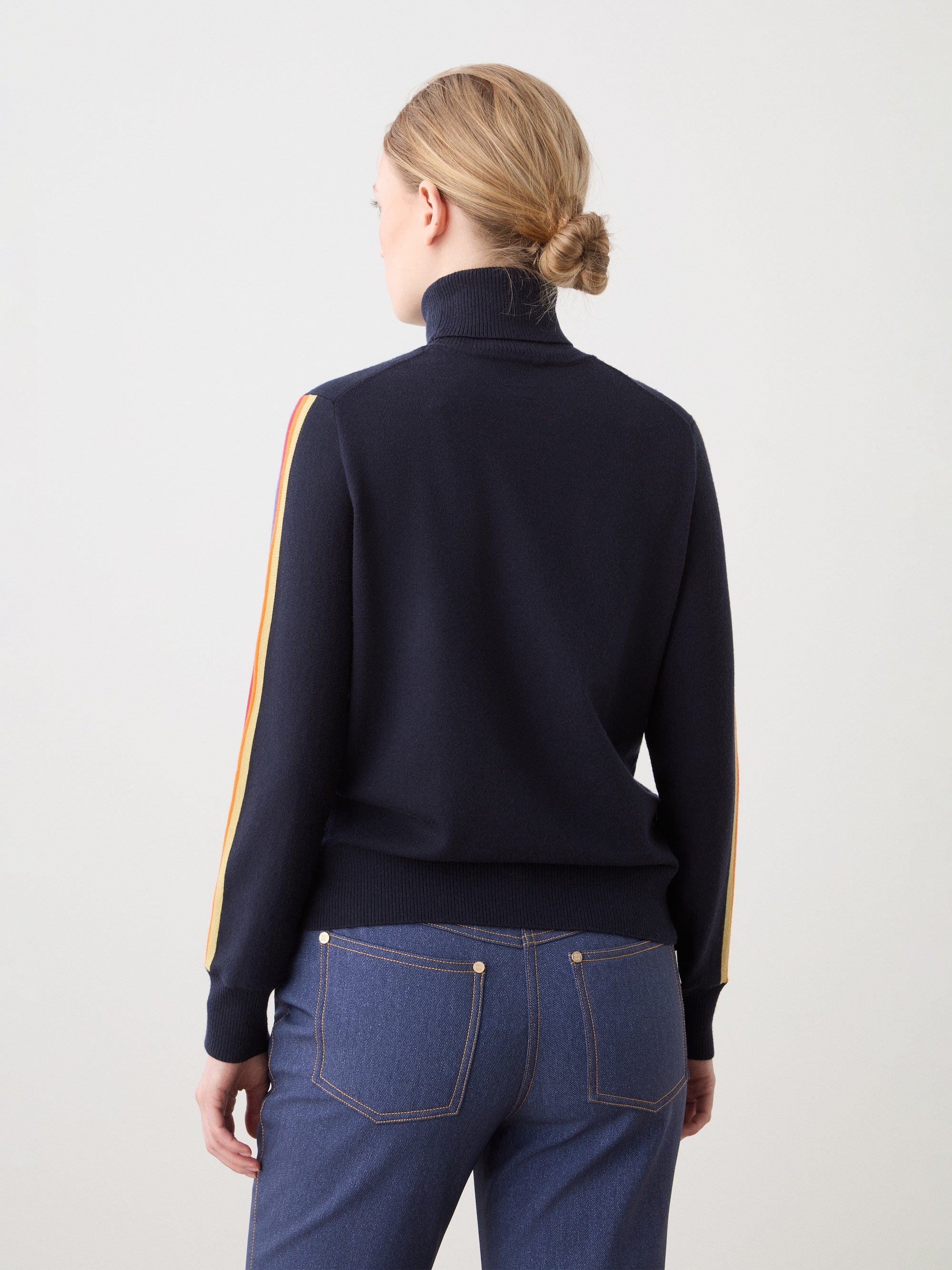 We Norwegians | FW25 | Womens Freebird Turtleneck Sweater_Navy blue | Model is wearing this knitted turtleneck sweater with contrasting panels on the sleeves - paired with the Western ski pants | Shot against an off-white background | Back