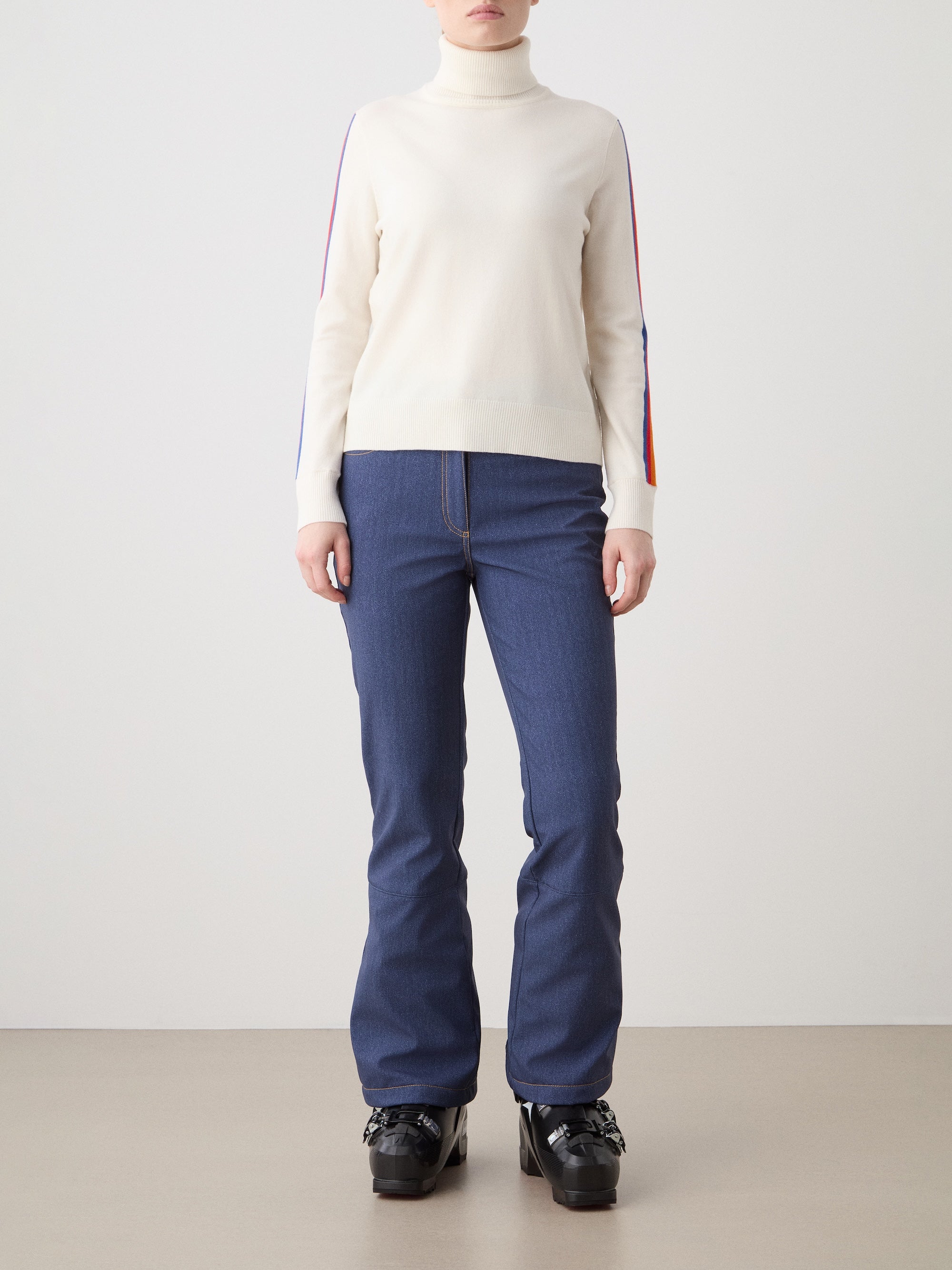 We Norwegians | FW25 | Womens Freebird Turtleneck Sweater_Off-white | Model is wearing this knitted turtleneck sweater with contrasting panels on the sleeves - paired with the Western ski pants | Shot against an off-white background | Front