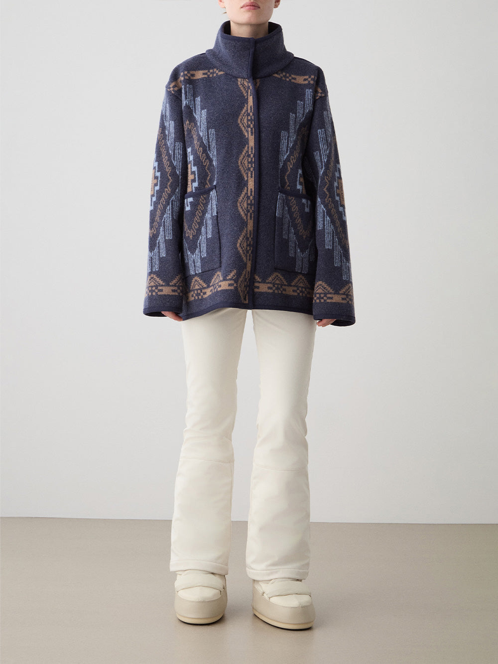 We Norwegians_FW25_Womens | Model is wearing the Navy blue Kautokeino jacket with Off white Tyin Bootleg Ski pants | The jacket come with a jacquard pattern inspired by Native and Indigenous American art | Front view against a white background