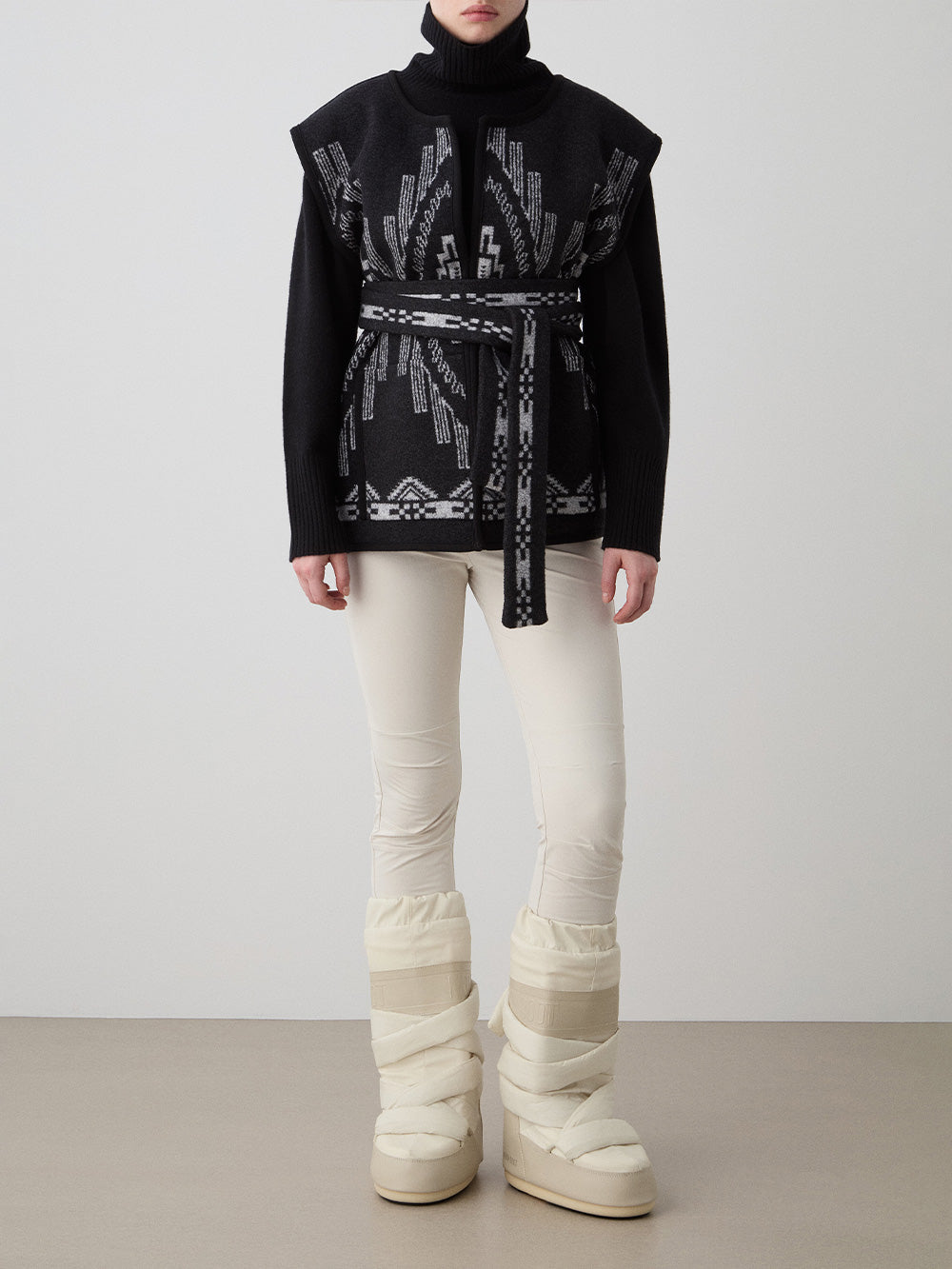We Norwegians_FW25_Women | Model is wearing the Kautokeino vest | Black in color with a jacquard pattern inspired by Native and Indigenous American Art | Vest has a matching belt to cinch the waist | Front view on a white background