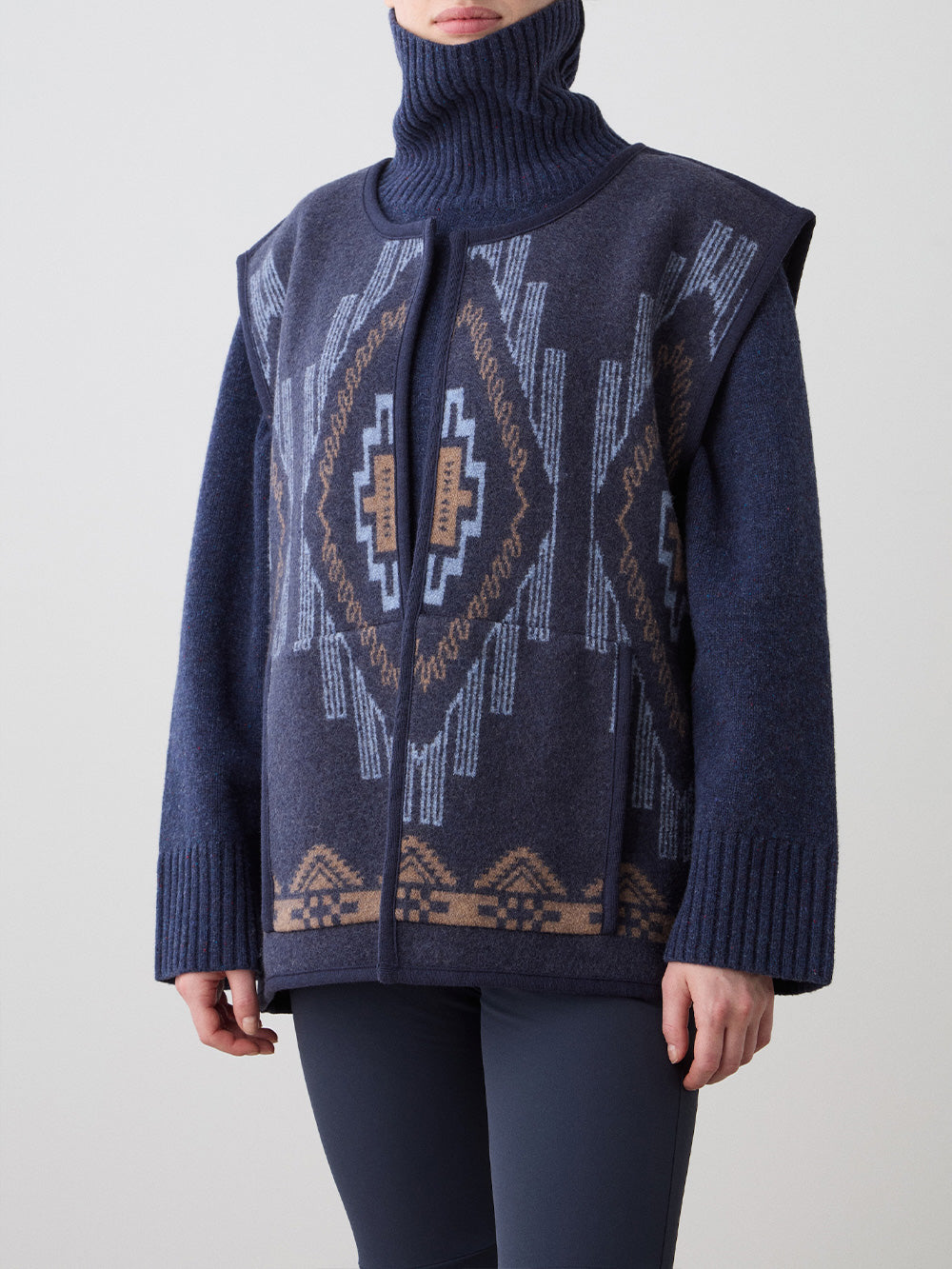 We Norwegians_FW25_Women | Model is wearing the Kautokeino vest | Navy blue in color with a jacquard pattern inspired by Native and Indigenous American Art | Vest has a matching belt to cinch the waist | Photograph is showing the details of the garment on a white background