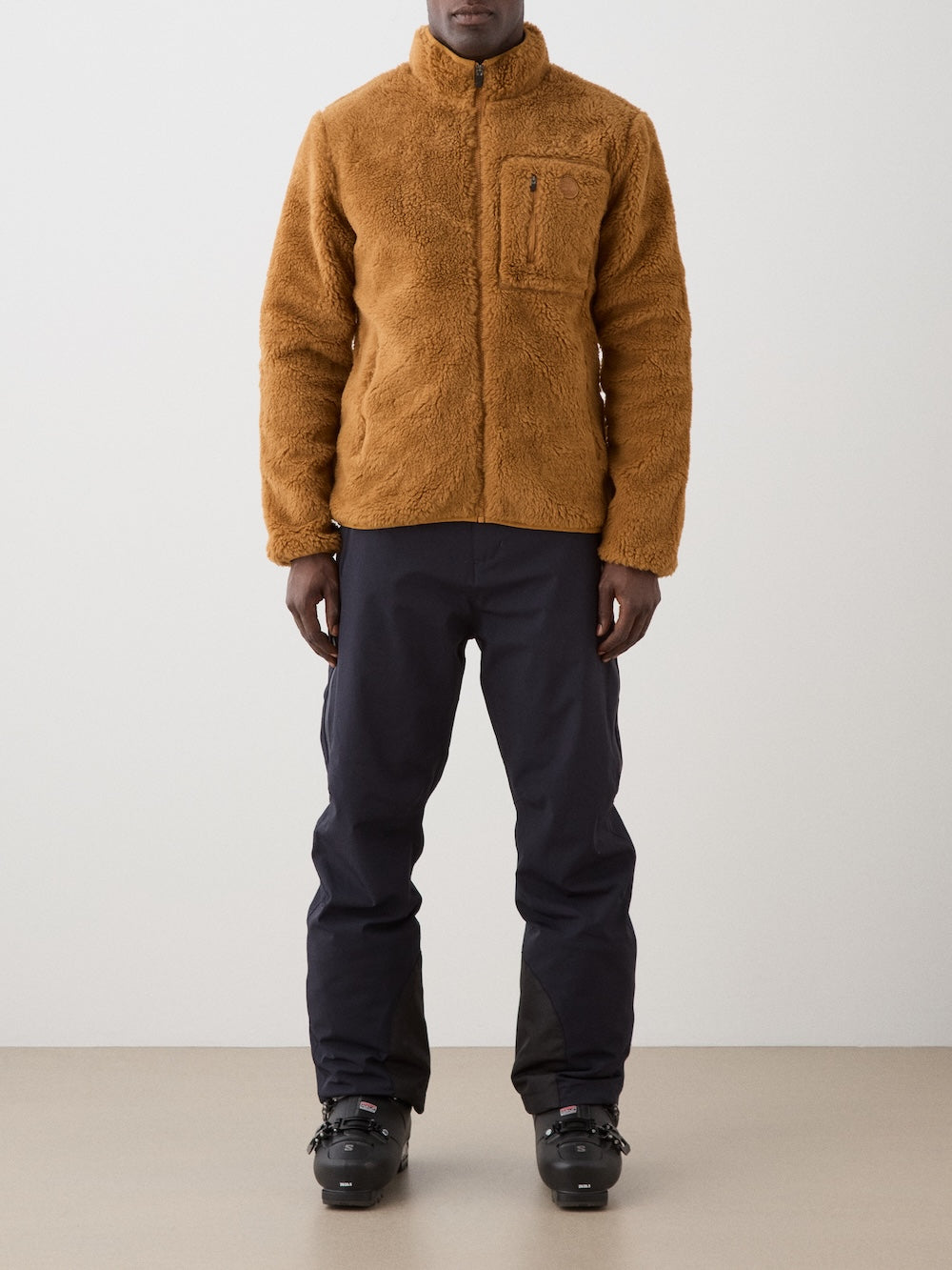 We Norwegians | FW25 | Mens Kebnekaise Jacket_Cinnamon | Model wearing this fleece jacket with front zipper opening, zipped chest pocket and side pockets - paired with black ski pants | Shot against an off-white background | Front