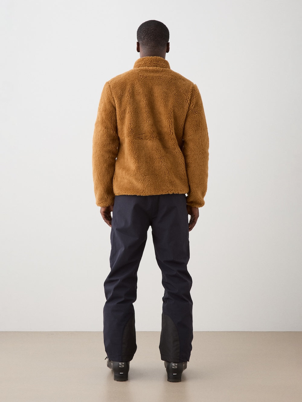 We Norwegians | FW25 | Mens Kebnekaise Jacket_Cinnamon | Model wearing this fleece jacket with front zipper opening, zipped chest pocket and side pockets - paired with black ski pants | Shot against an off-white background | Back