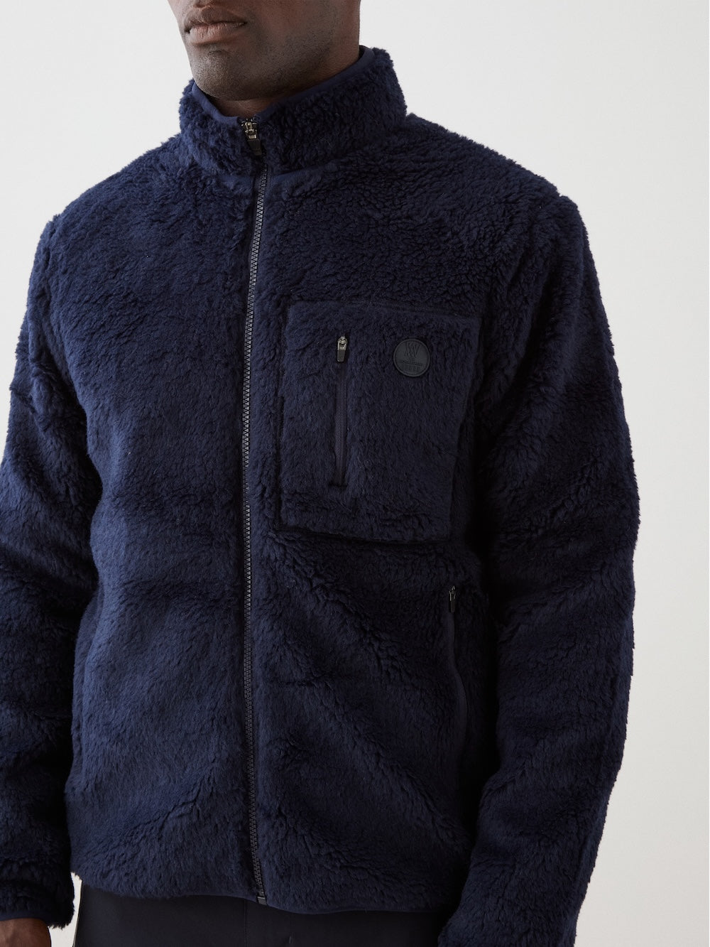 We Norwegians | FW25 | Mens Kebnekaise Jacket_Navy blue | Model wearing this fleece jacket with front zipper opening, zipped chest pocket and side pockets - paired with black ski pants | Shot against an off-white background | Close-up