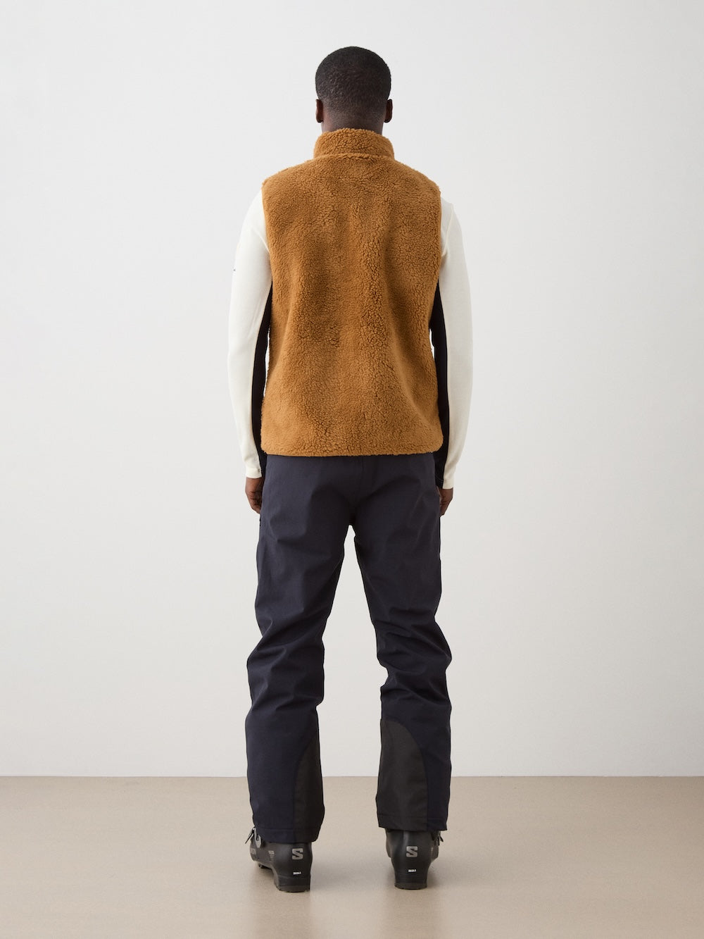 We Norwegians | FW25 | Mens Kebnekaise Vest_Cinnamon | Model wearing this fleece vest with front zipper opening, zipped chest pocket and side pockets -over an off-white top - paired with black ski pants | Shot against an off-white background | Back