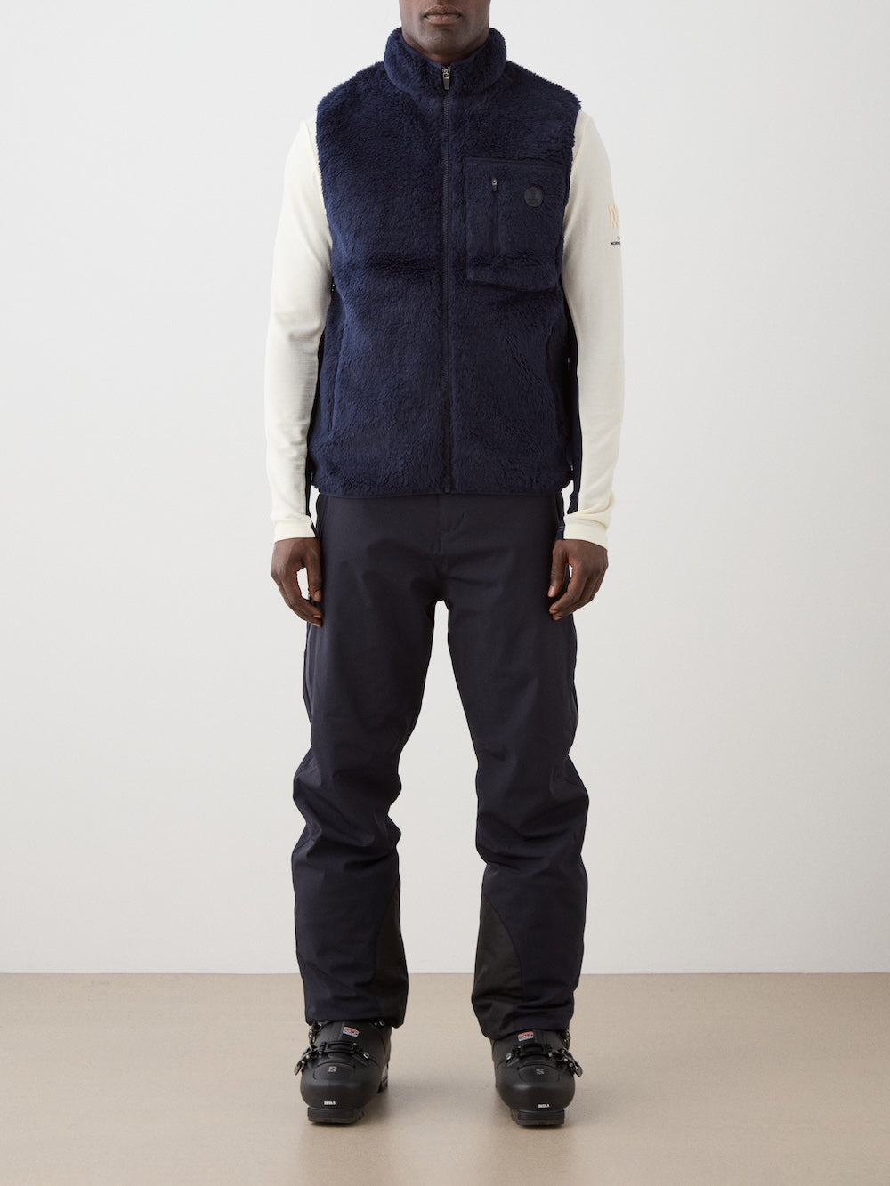 We Norwegians | FW25 | Mens Kebnekaise Vest_Navy blue | Model wearing this fleece vest with front zipper opening, zipped chest pocket and side pockets -over an off-white top - paired with black ski pants | Shot against an off-white background | Front