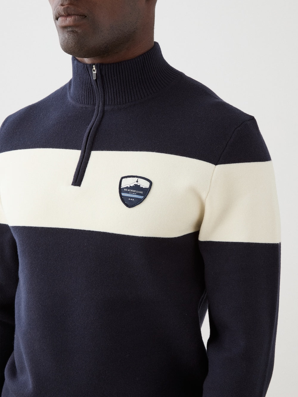 We Norwegians | FW25 | Mens Holmenkollen ZipUp_Navy blue | Model is wearing a merino/ cotton blend - knitted sweater with a 1/4th zipper opening and badge at the front | Shot against an off-white background | Close-up view