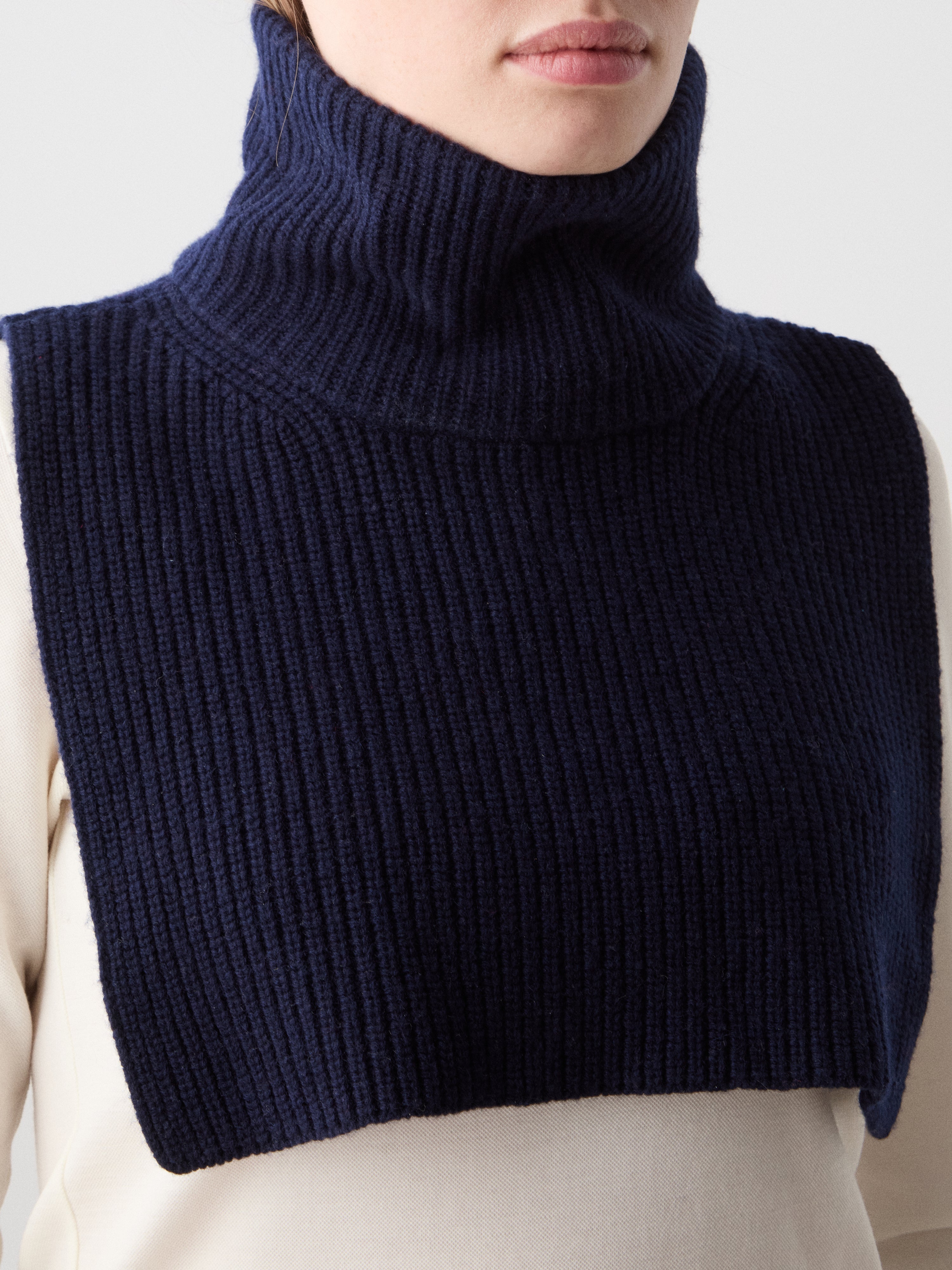 We Norwegians | FW25 | Dal Bib_Navy blue | Model wearing the knitted turtle neck bib over a white sweater | Shot against an off-white background