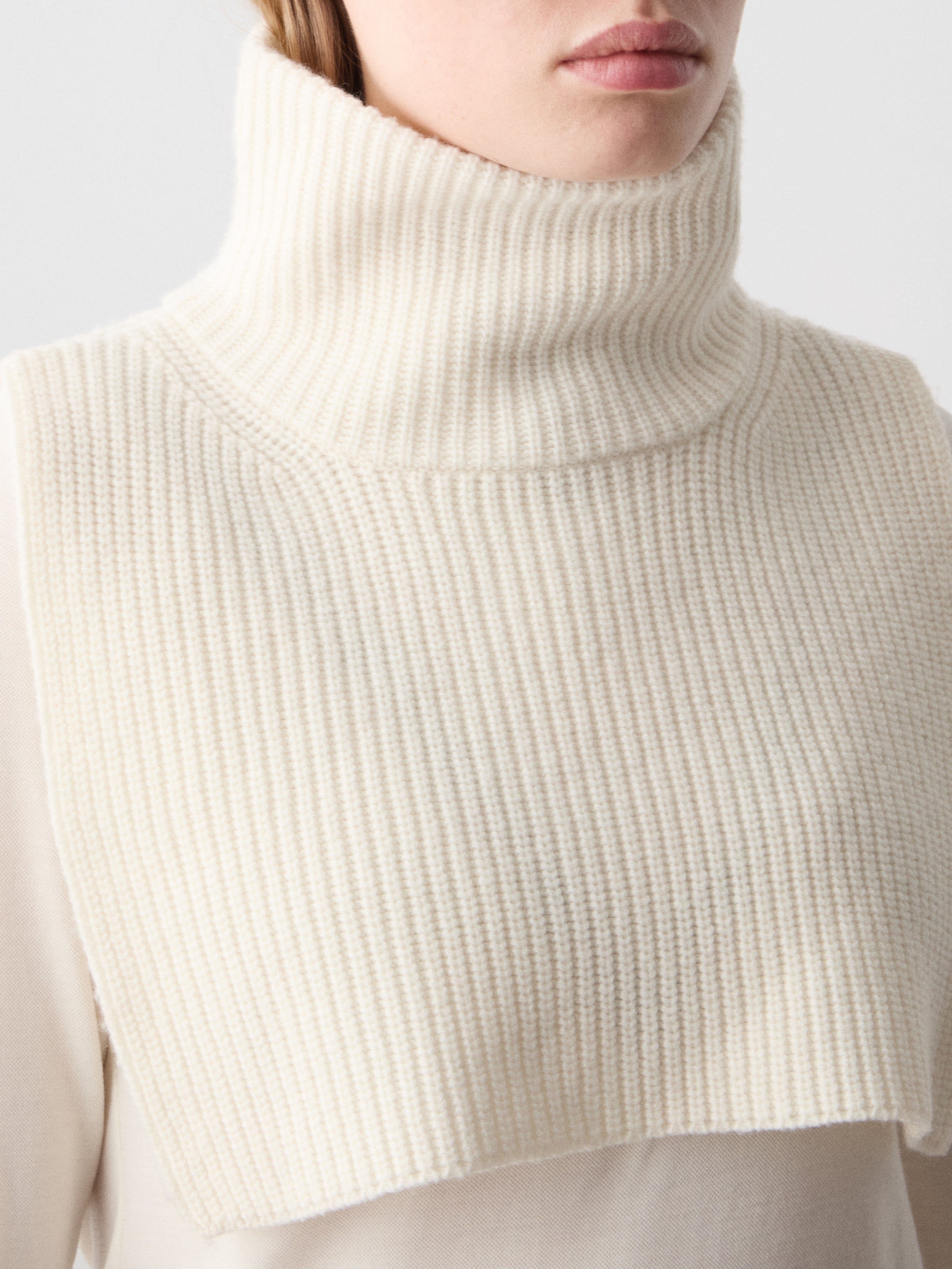 We Norwegians | FW25 | Dal Bib_Off white | Model wearing the knitted turtle neck bib over a white sweater | Shot against an off-white background