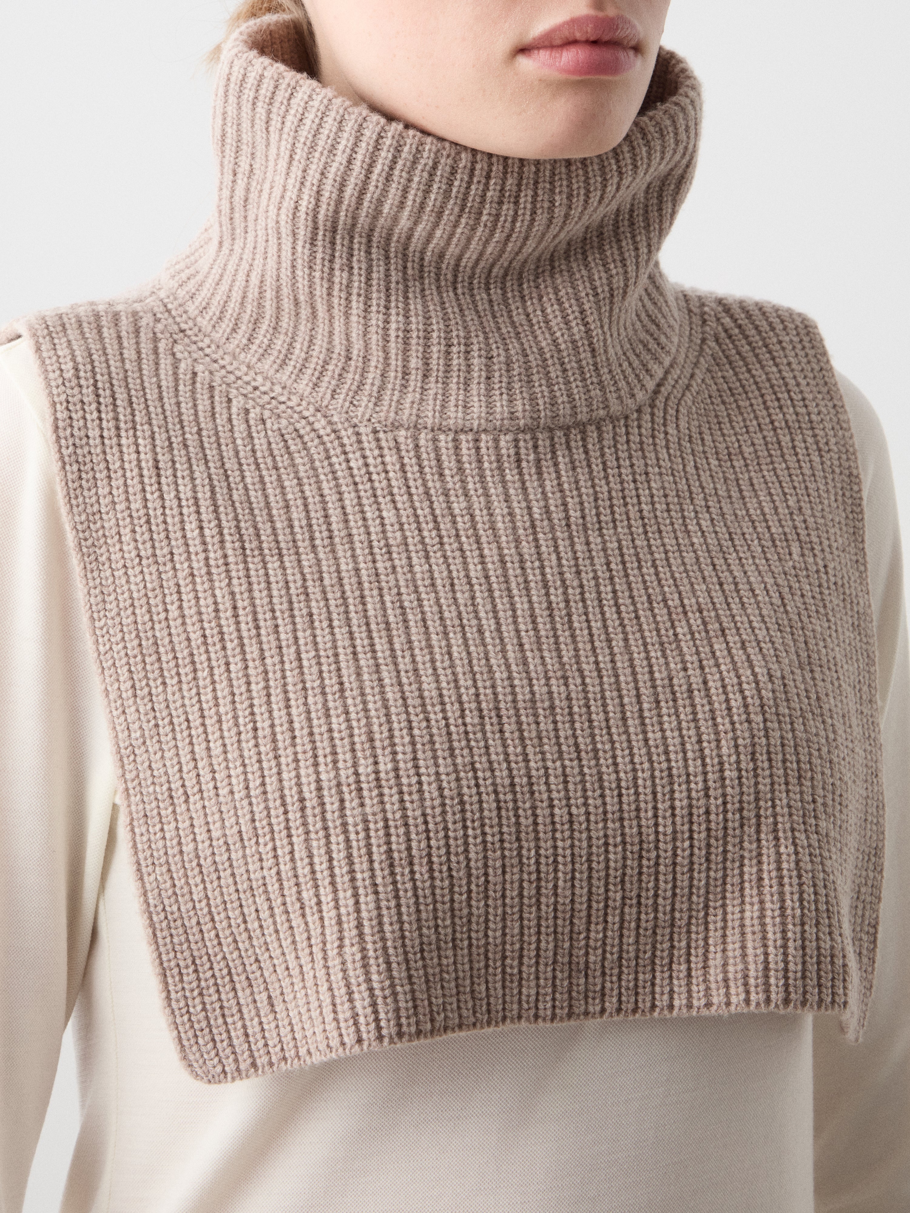 We Norwegians | FW25 | Dal Bib_Sand | Model wearing the knitted turtle neck bib over a white sweater | Shot against an off-white background