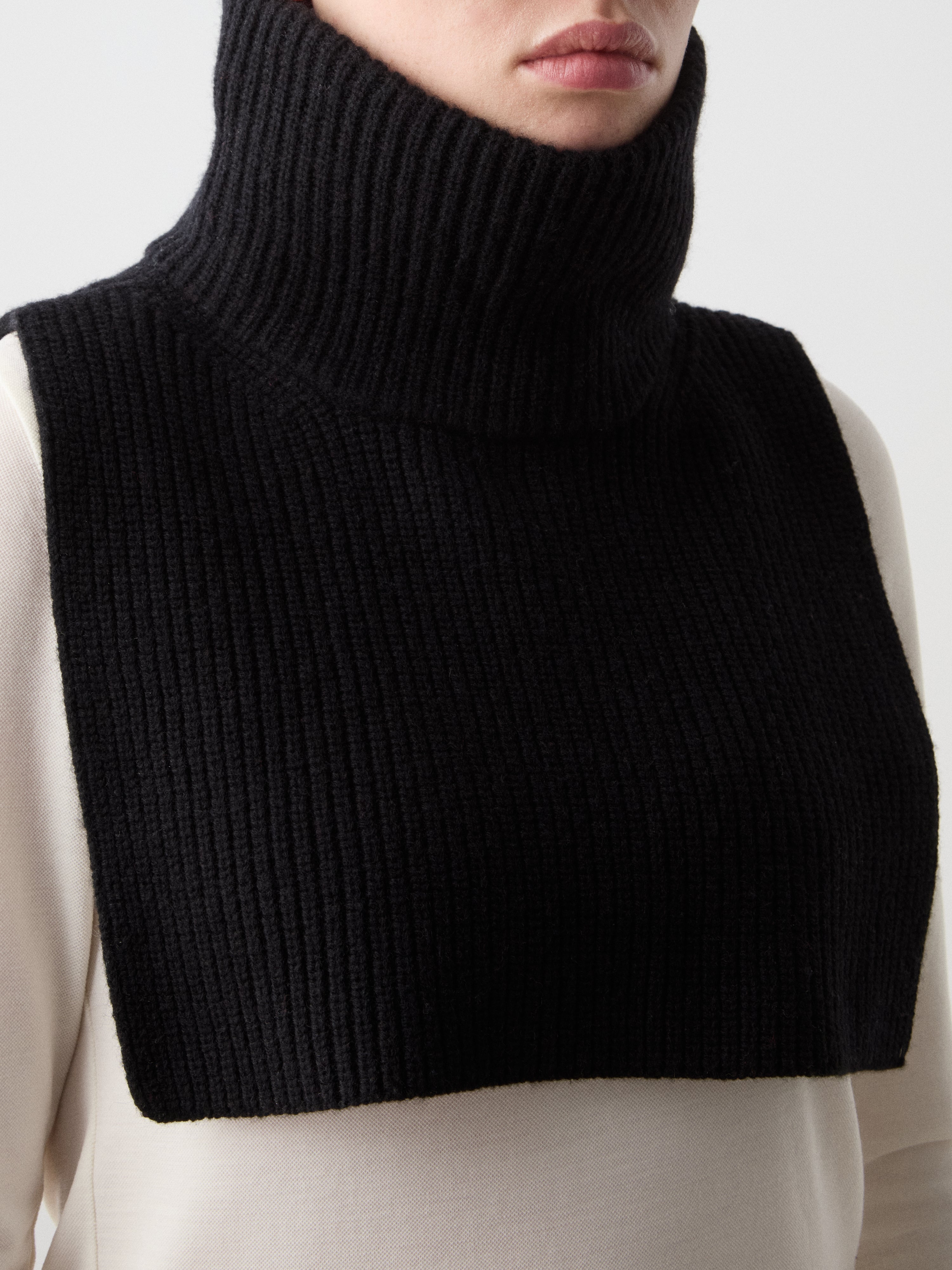 We Norwegians | FW25 | Dal Bib_Black | Model wearing the knitted turtle neck bib over a white sweater | Shot against an off-white background