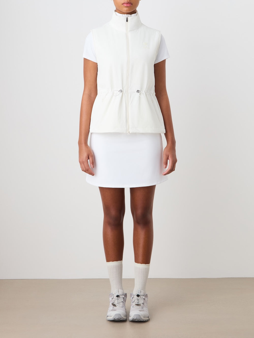 Person wearing a white vest, skirt, and shoes on a plain background