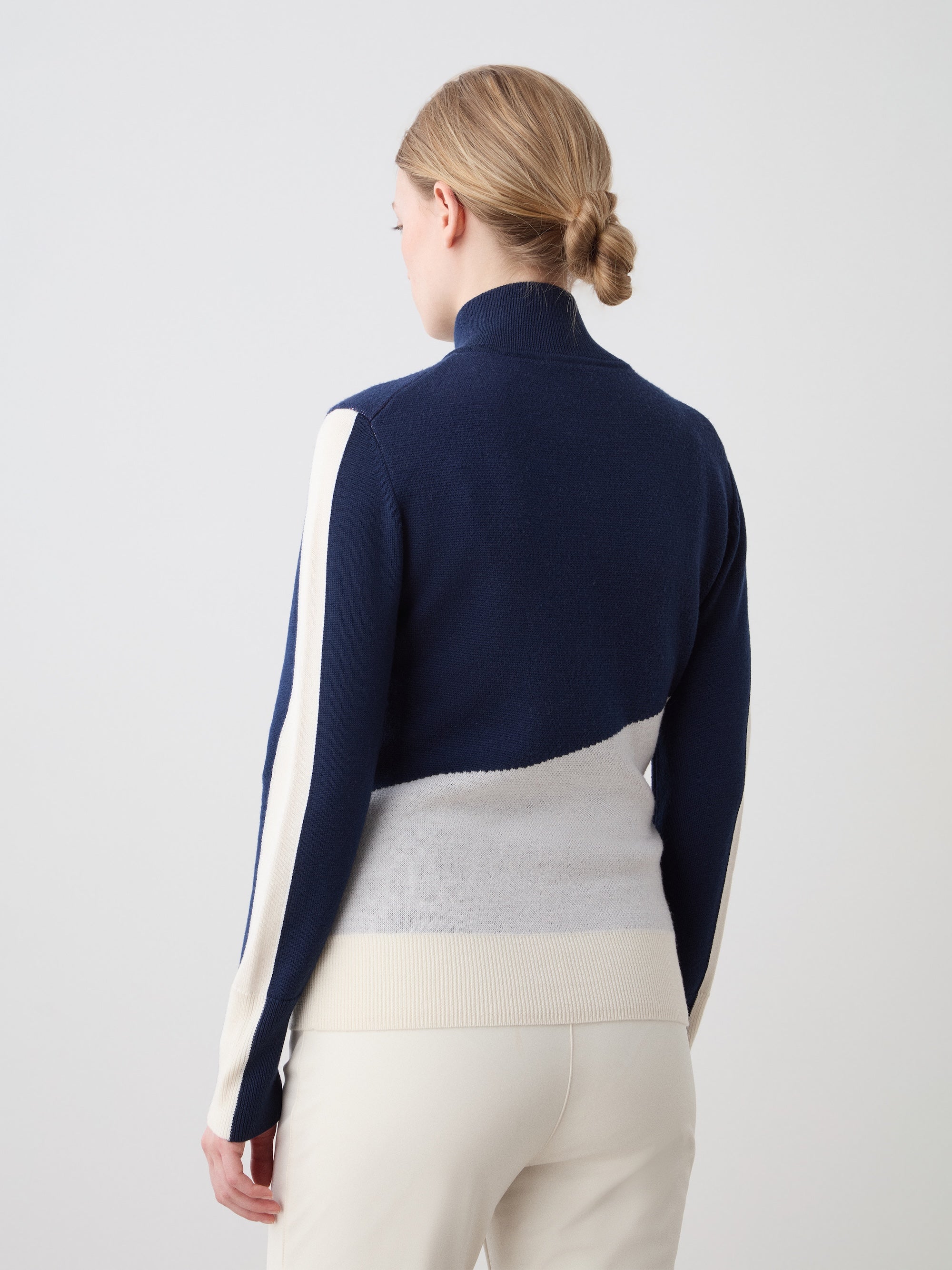 We Norwegians | FW25 | The model is wearing womens Afterski zip-up in navy blue which has the logo and 1/4th zipper in the front, against an off white background | Back view